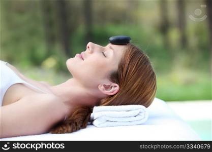 Woman laying on massage bed with hot stone on forehead