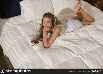 Woman laying on modern bed in bedroom in morning listening to music on headphones