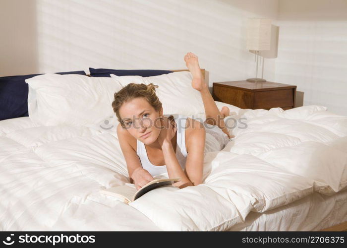 Woman laying on modern bed in bedroom in morning reading book