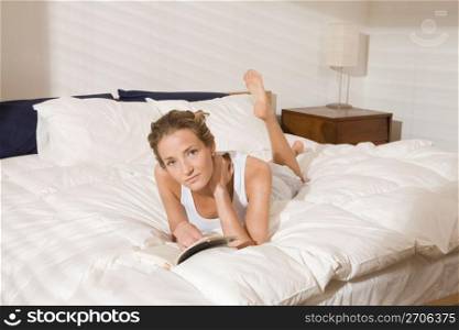 Woman laying on modern bed in bedroom in morning reading book