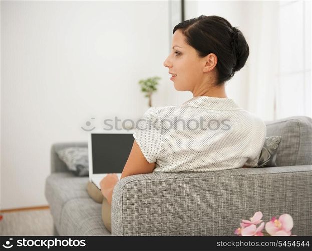 Woman laying on sofa and working on laptop. Rear view