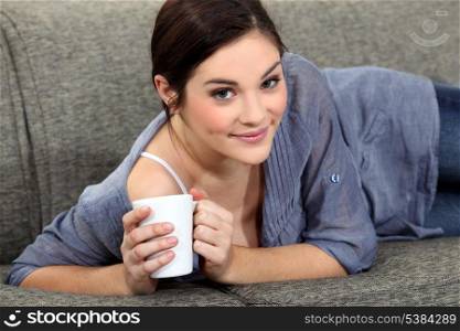 Woman laying on sofa with mug of coffee