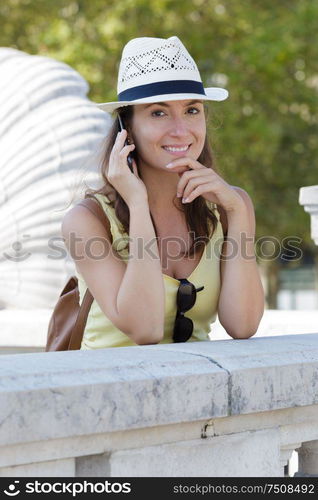 woman leaning on bridge and using mobile phone