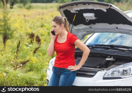 Woman leaning on broken car and calling for help by mobile phone