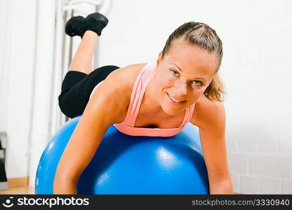 Woman leaning on top of a blue fitness ball having a break from her training looking at the viewer