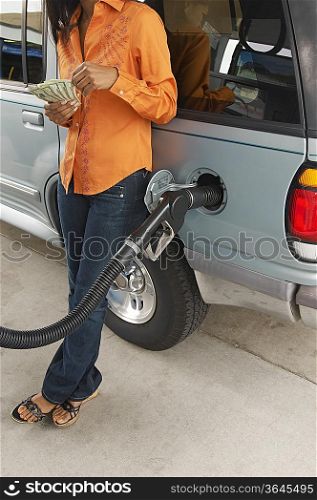 Woman leaning on van with fuel pump counting money, low section
