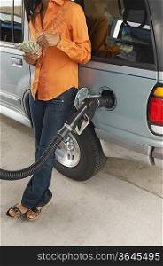 Woman leaning on van with fuel pump counting money, low section