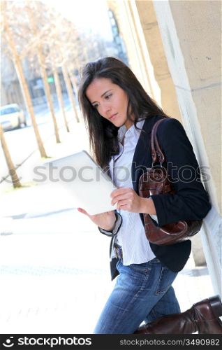 Woman leaning on wall in town with electronic tablet