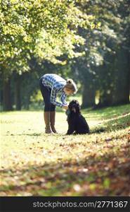 woman leaning over black dog on a walk in the park