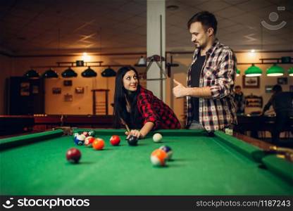 Woman learn to play billiard, poolroom on background. Couple hobby, american pool game, female player aiming to shot. Woman learn to play billiard, poolroom