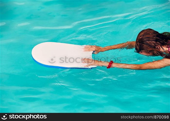 Woman learning to swim, practicing in swimming pool using a board. Candid people, real moments, authentic situations