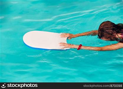 Woman learning to swim, practicing in swimming pool using a board. Candid people, real moments, authentic situations