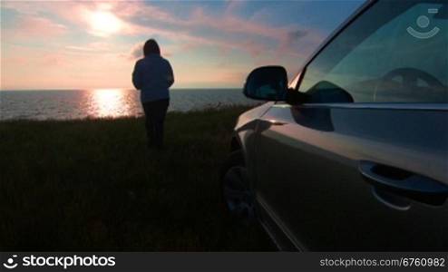 Woman left the car, strolling in the direction of the sea shore at sunset
