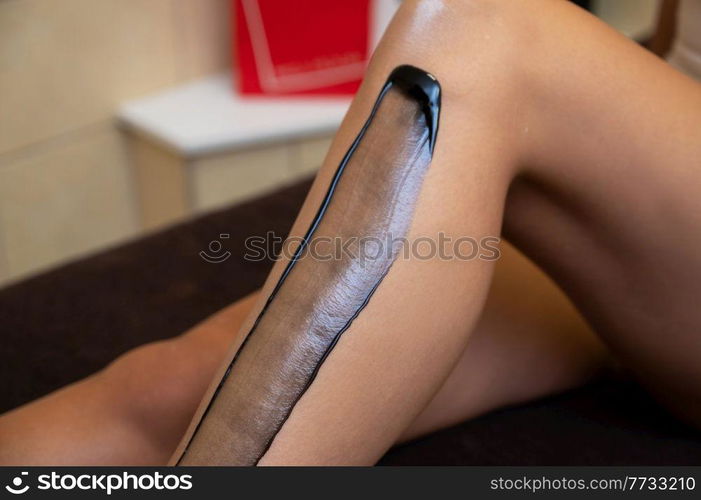 Woman legs closeup in beauty clinic ready for removing hair procedure using a black shugaring paste. Beauty and body care concept.. Woman legs closeup in beauty clinic ready for removing hair procedure