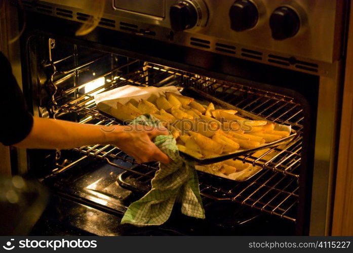 Woman lifting a tray of potato wedges into oven