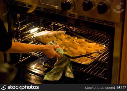 Woman lifting a tray of potato wedges into oven