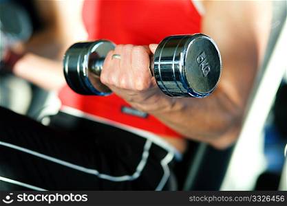 Woman lifting hand weights in a gym, in the background a man doing the same; focus on hand of woman