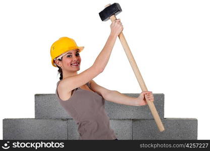 Woman lifting sledge-hammer in front of unfinished wall