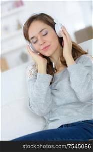 woman listening music in headphones sitting on sofa in room