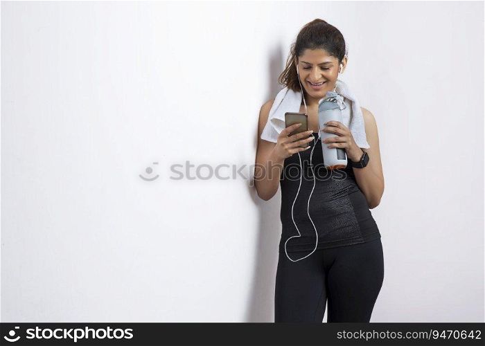 Woman listening to music on her phone while holding her water bottle after a workout and smiling. 