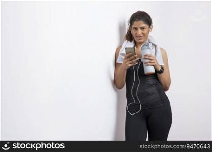 Woman listening to music on her phone while holding her water bottle after a workout and smiling. 