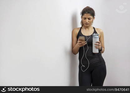 Woman listening to music on her phone while holding her water bottle after a workout. 