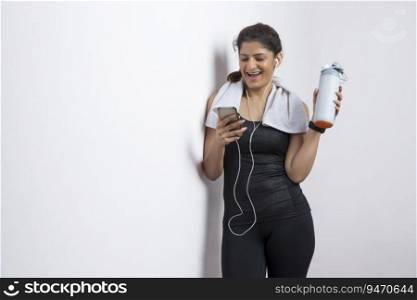 Woman listening to music on her phone while holding her water bottle after a workout. 