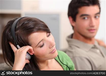 Woman listening to music through headphones boyfriend watching