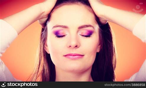 Woman long straight hair closed eyes with colorful shadows vivid color makeup portrait studio shot on orange background