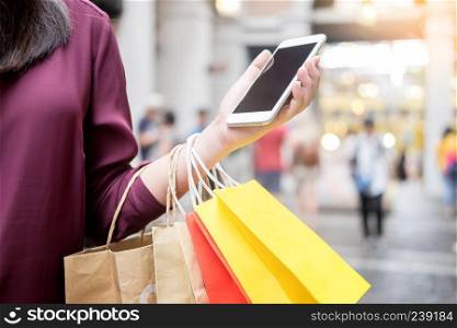 Woman look at mobile phone with paperbags in the mall while enjoying a day shopping