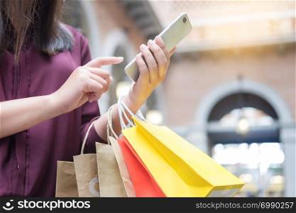 Woman look at mobile phone with paperbags in the mall while enjoying a day shopping