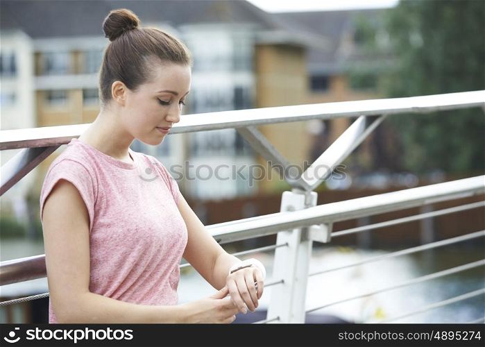 Woman Looking At Activity Tracker Whilst Exercising In City