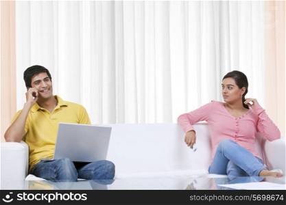 Woman looking at boyfriend talking on mobile phone while using laptop