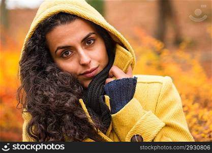 Woman looking at camera in hooded coat in fall forest