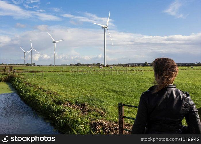 Woman looking at dutch landscape, windmills and cows in the distance with blue sky ,meadow. Woman looking at dutch landscape, windmills and cows in the distance with blue sky