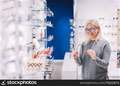 Woman looking at glasses at optic store. Shopping, choosing eyewear. Vision defect.. Woman looking at glasses at optic store.