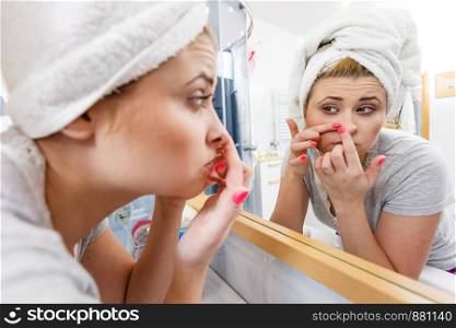Woman looking at her reflection in mirror thinking about her complexes having serious face expression, analyzing face skin complexion squeezing pimples. Woman looking in mirror dealing with acne