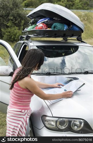 Woman looking at map on the car hood in the mountain.