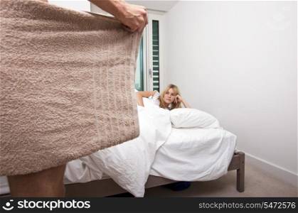 Woman looking at nude man holding towel in bedroom
