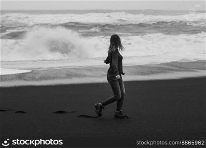 Woman looking at stormy sea on beach monochrome scenic photography. Picture of person with splashing waves on background. High quality wallpaper. Photo concept for ads, travel blog, magazine, article. Woman looking at stormy sea on beach monochrome scenic photography