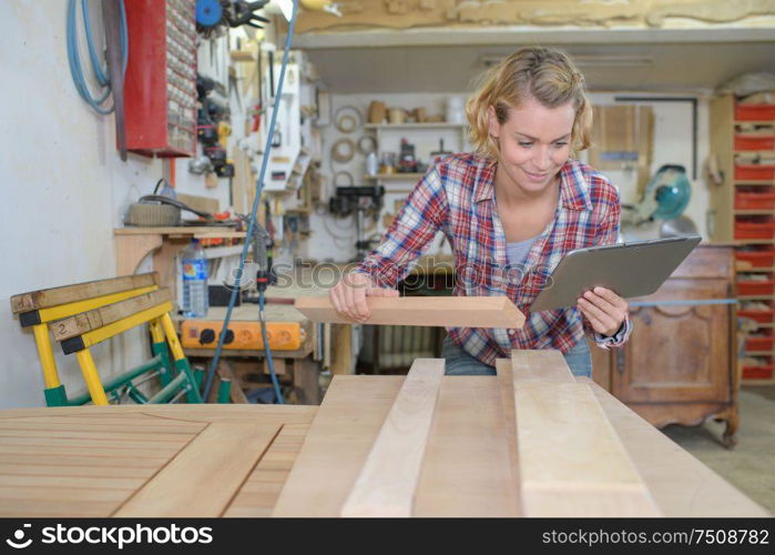woman looking at tablet while working with wood