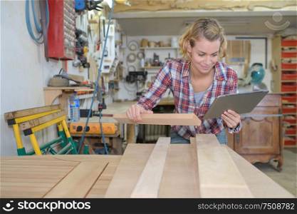 woman looking at tablet while working with wood