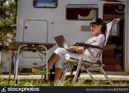 Woman looking at the laptop near the camping . Caravan car Vacation. Family vacation travel, holiday trip in motorhome RV. Wi-fi connection information communication technology.
