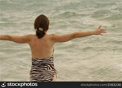 Woman looking at the ocean with her arms stretching