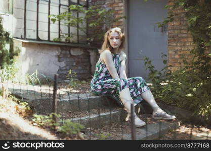 Woman looking away and sitting on doorstep scenic photography. Picture of lady with abandoned greenhouse on background. High quality wallpaper. Photo concept for ads, travel blog, magazine, article. Woman looking away and sitting on doorstep scenic photography