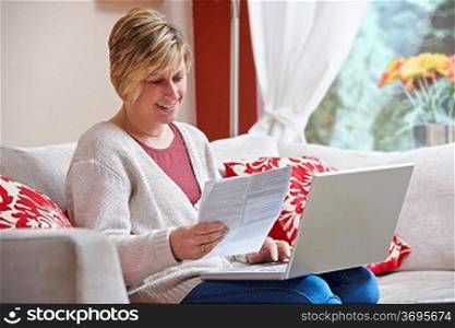 Woman looking happy while sitting at home doing home banking with laptop