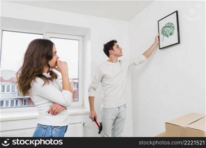 woman looking his boyfriend hanging picture frame white wall