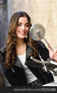 Woman looking in a motorbike&rsquo;s mirror, smiling and wearing casual clothes