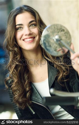 Woman looking in a motorbike&rsquo;s mirror, smiling and wearing casual clothes