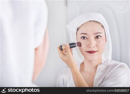 woman looking in the mirror and applying cosmetic with a brush